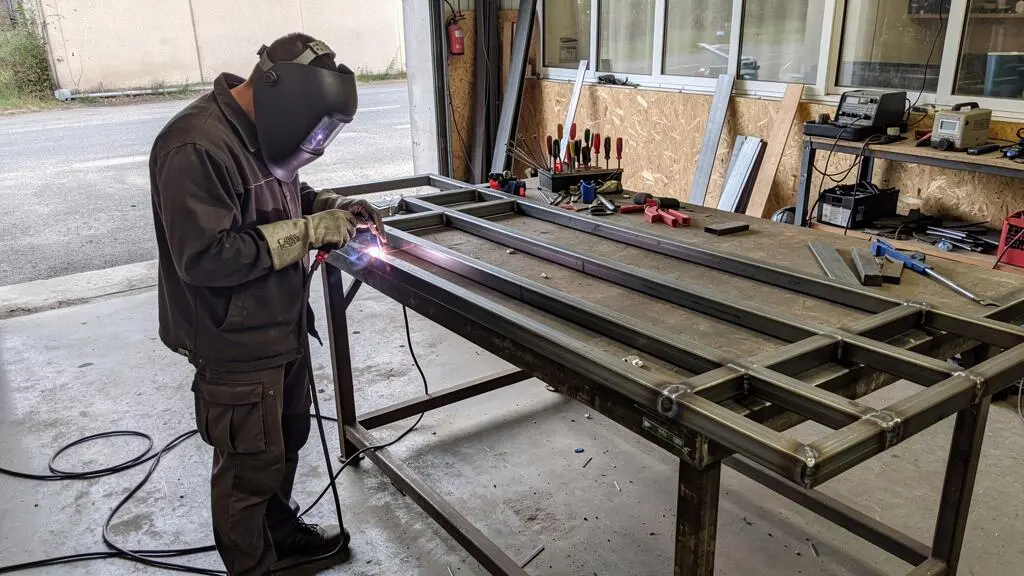 Soudeur débutant travaillant sur un portail en acier simple dans un atelier, projet d'apprentissage pratique visible